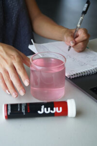 A glass of Juju collagen with vitamin c about to be consumed by a man writing on the table.