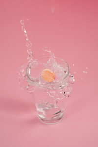 fizz tablets dropped in a glass of water in pink background