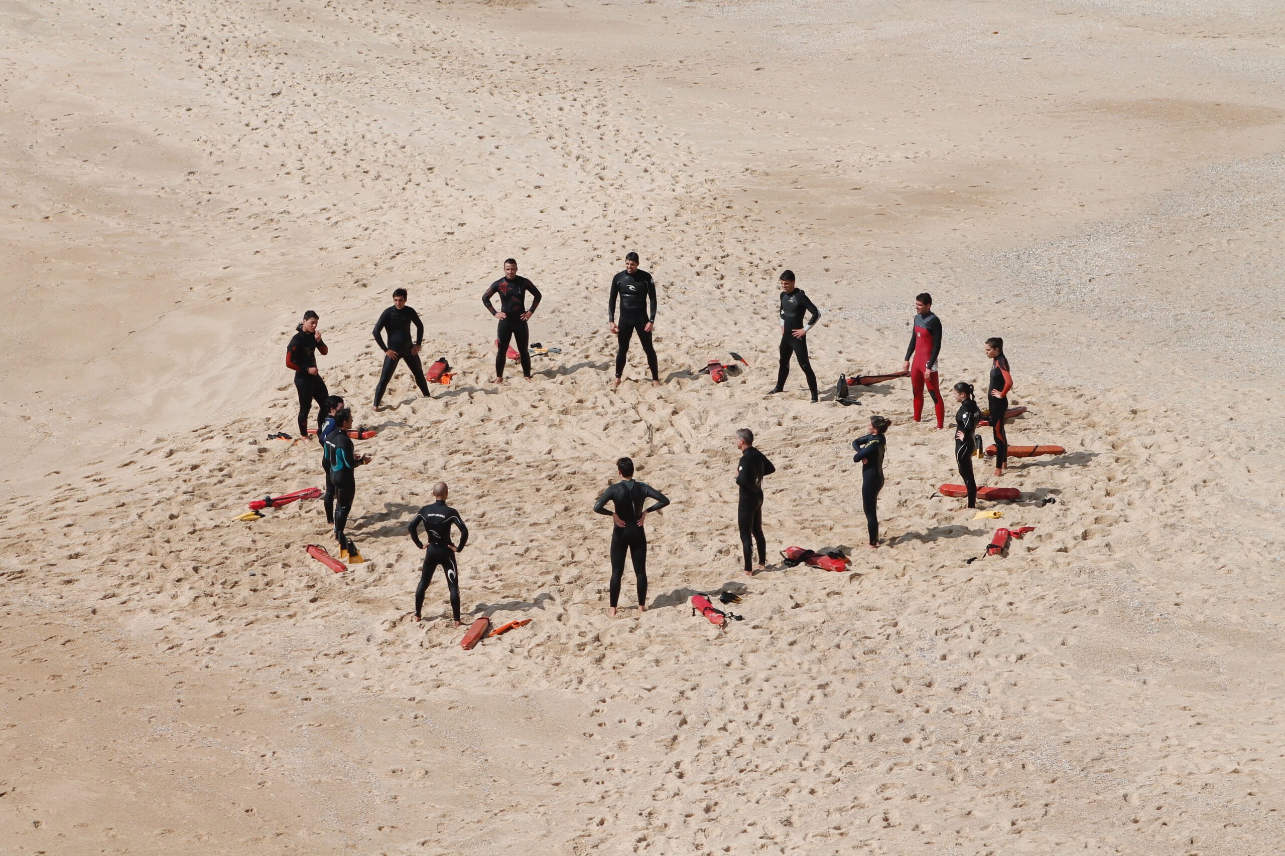 Group of 14 people doing hip circle exercises on the beach.