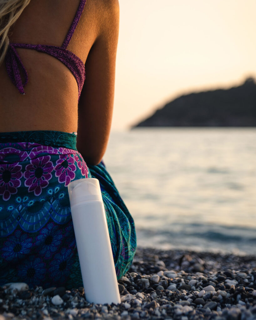 Woman sitting on the beach with peeling lotion beside her and this is for our guide on peeling lotion benefits.